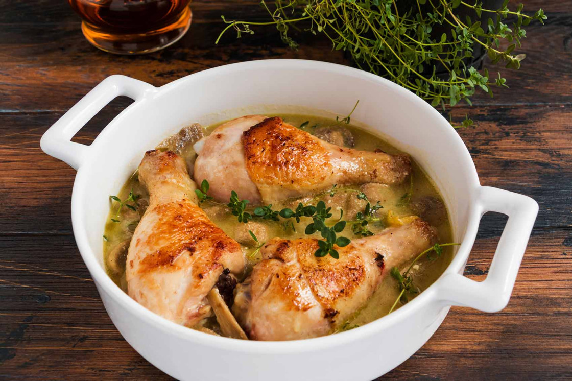 Delicious chicken drumsticks in creamy sauce, garnished with thyme, served in a rustic dish.
