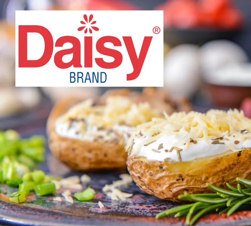 Daisy Brand sour cream and shredded cheese topping loaded baked potatoes garnished with rosemary and green onion.