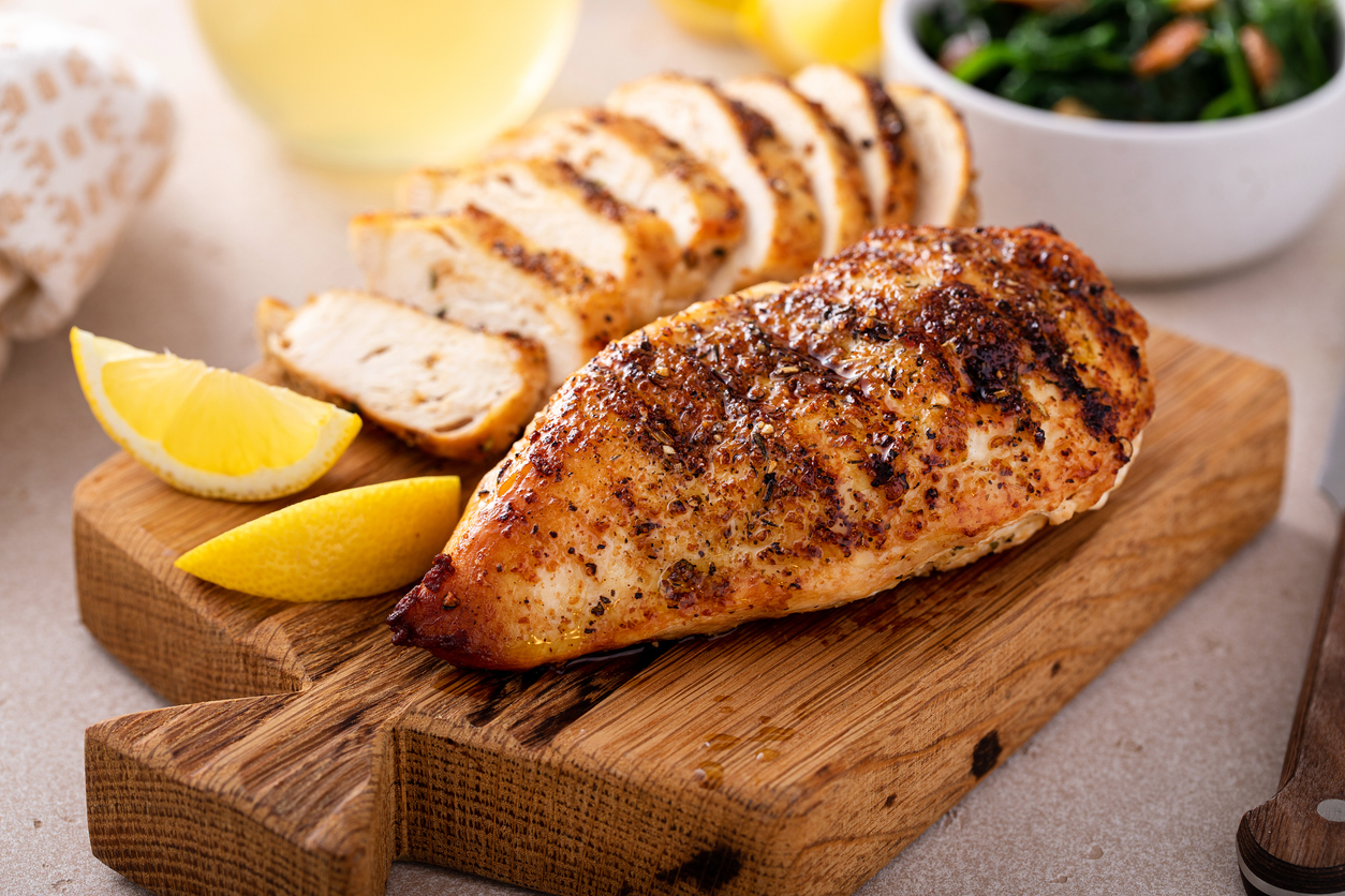 Grilled Chicken Breast Whole And Sliced On A Cutting Board With Lemon