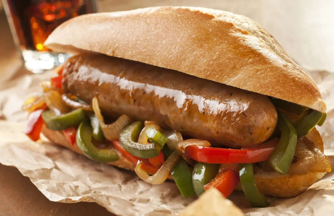 Grilled sausage sandwich with sautéed green peppers, red peppers, and onions on toasted bun, ideal for foodservice suppliers.