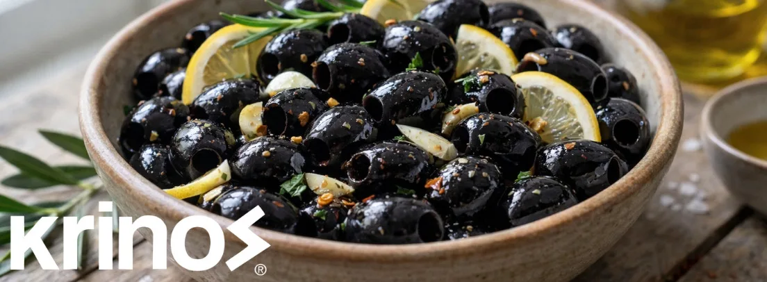 Premium Krinos black olives in earthenware bowl, garnished with fresh lemon slices and rosemary sprigs, ideal for foodservice wholesale.