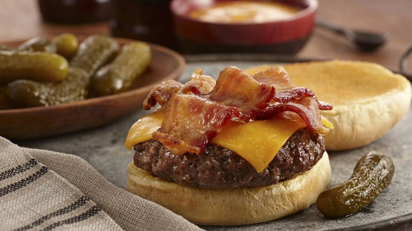 Gourmet bacon cheeseburger featuring melted cheese and crispy bacon strips on a soft bun, ideal for wholesale food service and commercial food suppliers.