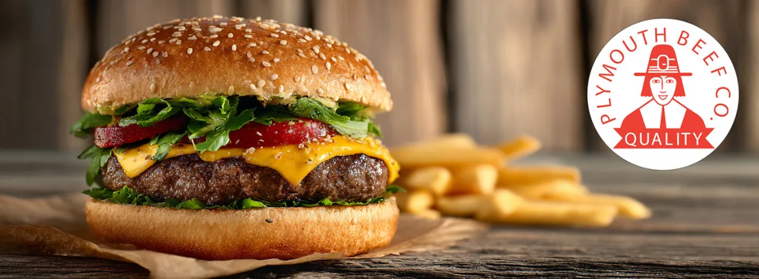 Professional food photography of a gourmet beef burger with melted cheese, fresh lettuce, and tomato on sesame seed bun, served with golden fries. Plymouth Beef Co quality branding visible.