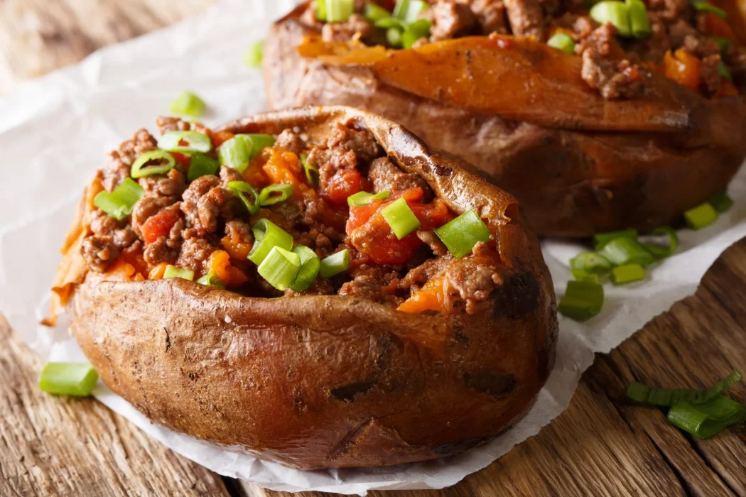 Baked potato halves filled with seasoned ground beef, diced peppers, and green onions for foodservice meal preparation and wholesale distribution.